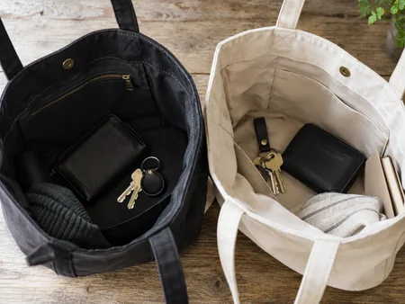 Two tote interiors viewed from above, one dark lining and one pale lining with keys and a small black wallet inside each.
