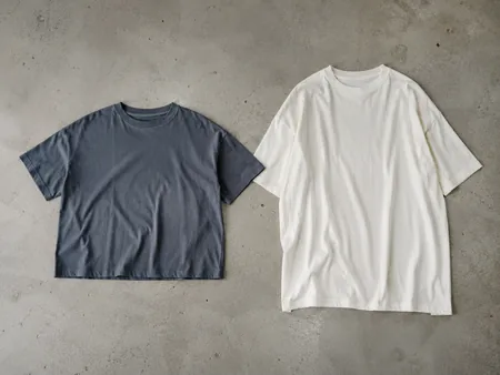 Two plain T-shirts laid flat side by side: one short broad boxy shirt, one longer oversized shirt with dropped shoulder seams. Whole garments visible.