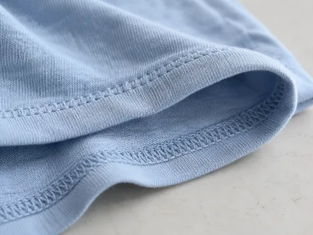 Macro photograph of a pale blue cotton jersey T-shirt edge folded back, clearly showing fine knitted loops and soft drape.